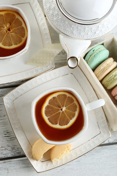 Macaron colorati con teiera e tazza di tè su sfondo di legno a colori — Foto Stock