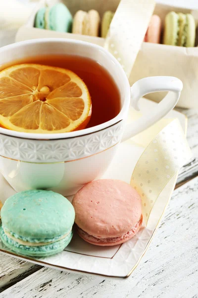 Macarons colorés avec tasse de thé sur fond de bois de couleur — Photo