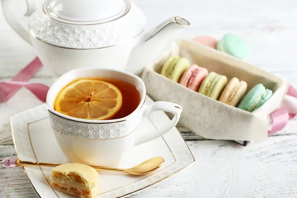 Macaroons coloridos com xícara de chá na tabela de madeira da cor, no fundo claro — Fotografia de Stock