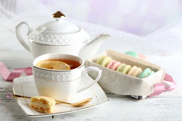 Macaroons coloridos com xícara de chá na tabela de madeira da cor, no fundo claro — Fotografia de Stock