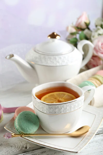 Bunte Makronen mit Tasse Tee auf farbigem Holztisch, auf hellem Hintergrund — Stockfoto