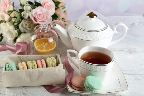 Bunte Makronen mit Tasse Tee auf farbigem Holztisch, auf hellem Hintergrund — Stockfoto