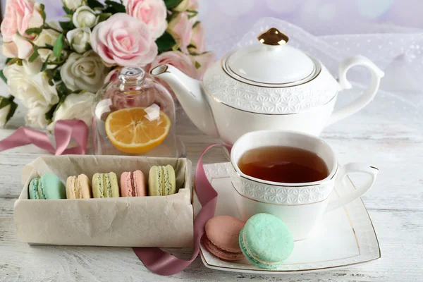 Macarrones coloridos con taza de té en la mesa de madera de color, sobre fondo claro — Foto de Stock