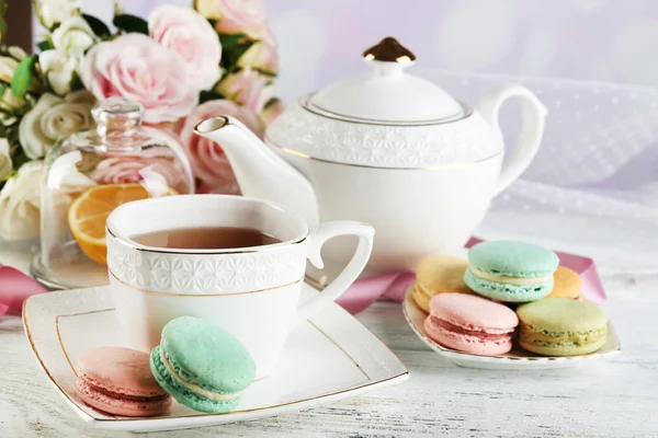 Macarrones coloridos con taza de té en la mesa de madera de color, sobre fondo claro —  Fotos de Stock