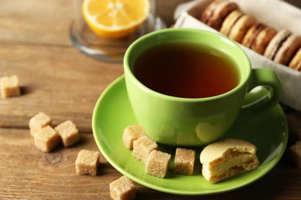 Bunte Makronen mit Tasse Tee auf hölzernem Hintergrund — Stockfoto