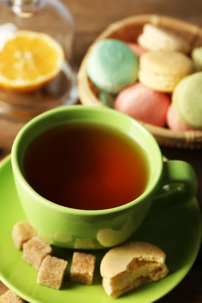 Bunte Makronen mit Tasse Tee auf hölzernem Hintergrund — Stockfoto