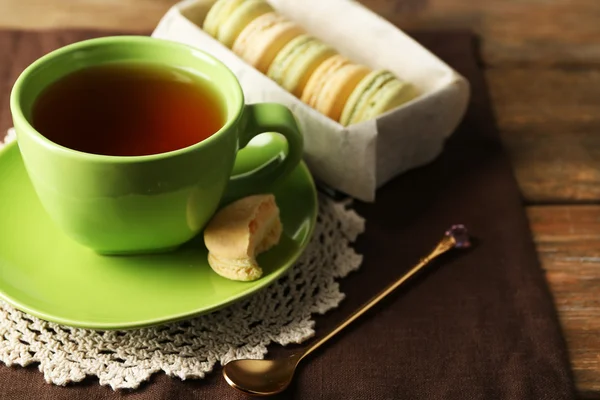 Kleurrijke bitterkoekjes met kopje thee op houten achtergrond — Stockfoto