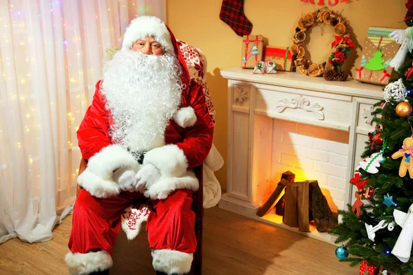 Santa claus zittend in een comfortabele stoel in de buurt van open haard thuis — Stockfoto