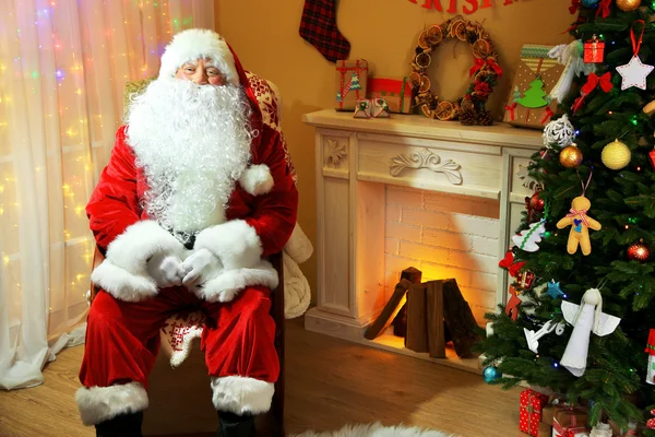 Santa Claus sitting in comfortable chair near fireplace at home — Stock Photo, Image