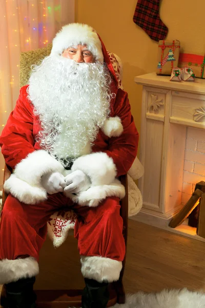 Santa claus zittend in een comfortabele stoel in de buurt van open haard thuis — Stockfoto