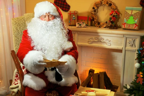 Santa claus zitten met kinderen brieven in comfortabele stoel in de buurt van open haard thuis — Stockfoto