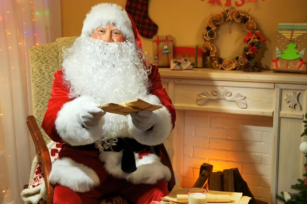 Santa claus zitten met kinderen brieven in comfortabele stoel in de buurt van open haard thuis — Stockfoto