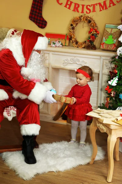 Santa Claus giving  present to  little cute girl near  fireplace and Christmas tree at home — Stock Photo, Image