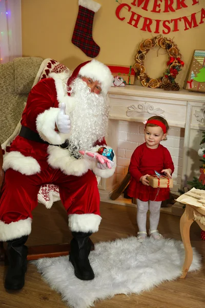 Santa Claus att ge närvarande att lilla söta tjejen nära spis och julgran hemma — Stockfoto