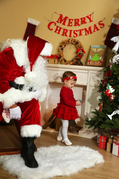 Babbo Natale che dà regalo alla bambina carina vicino al camino e all'albero di Natale a casa — Foto Stock