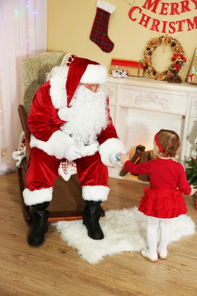 Weihnachtsmann beschenkt kleines süßes Mädchen am Kamin und Weihnachtsbaum zu Hause — Stockfoto