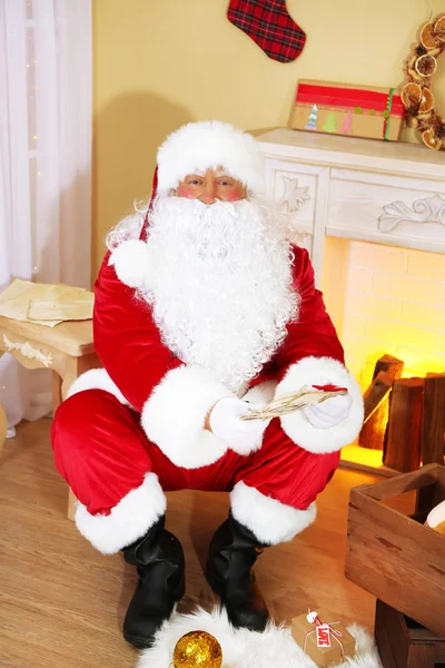 Papai Noel sentado em cadeira confortável perto de lareira em casa — Fotografia de Stock