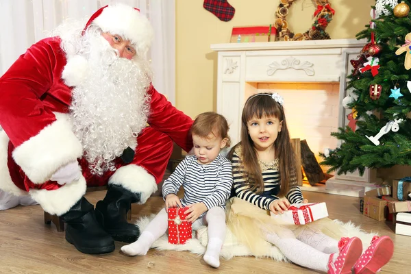 Père Noël avec deux petites filles mignonnes près de la cheminée et l'arbre de Noël à la maison — Photo