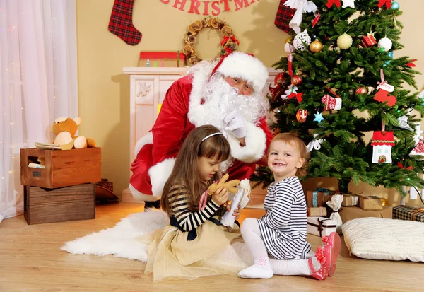 Santa Claus with two little cute girls near  fireplace and Christmas tree at home — Stock Photo, Image