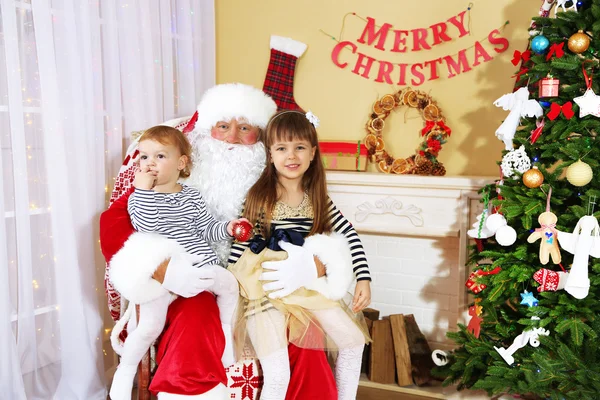 Papai Noel com duas meninas bonitos perto de lareira e árvore de Natal em casa — Fotografia de Stock