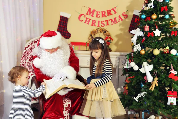 Libro di lettura di Babbo Natale con due bambine carine vicino al camino e all'albero di Natale a casa — Foto Stock