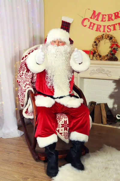 Santa claus zittend in een comfortabele stoel in de buurt van open haard thuis — Stockfoto