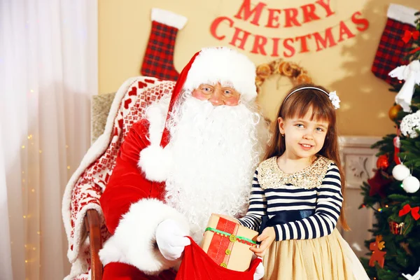 Noel Baba, evdeki Noel ağacının yanındaki küçük tatlı kıza hediye veriyor. — Stok fotoğraf