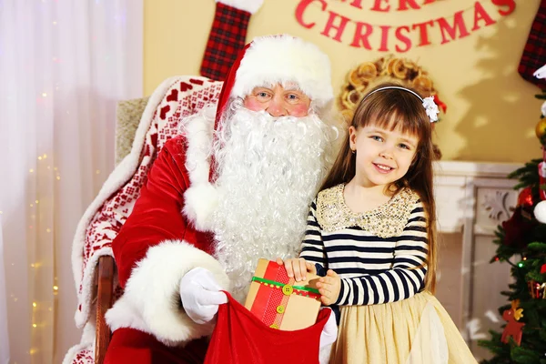 Weihnachtsmann beschenkt kleines süßes Mädchen in der Nähe des Weihnachtsbaums zu Hause — Stockfoto