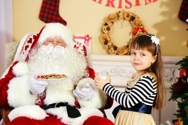 Lilla söta tjejen ger glas mjölk till jultomten nära julgran hemma — Stockfoto