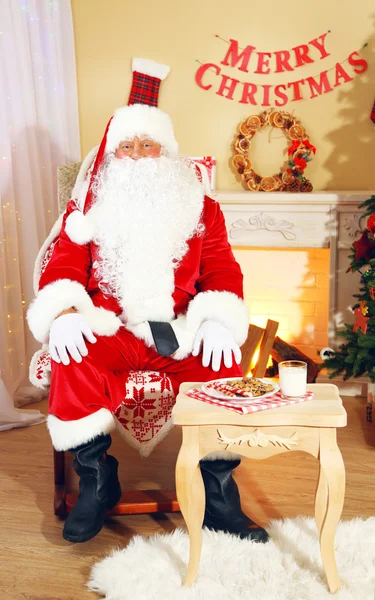 Babbo Natale seduto in comoda sedia vicino al camino a casa — Foto Stock