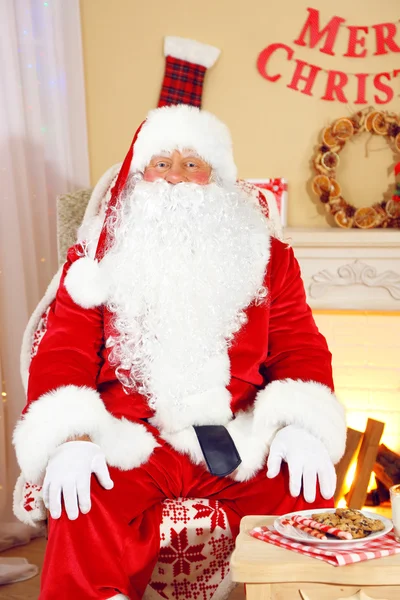 Santa claus zittend in een comfortabele stoel in de buurt van open haard thuis — Stockfoto