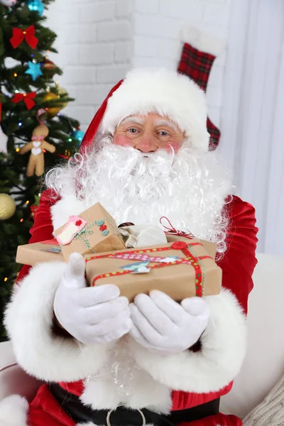 Weihnachtsmann sitzt auf Sofa mit Geschenkschachteln neben Weihnachtsbaum — Stockfoto