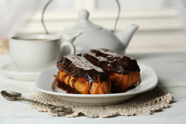 Eclares saborosos e xícara de chá na mesa de madeira — Fotografia de Stock