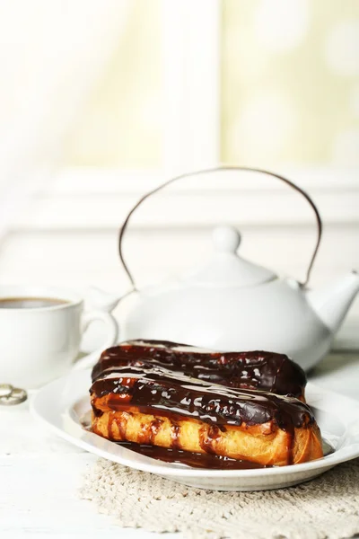 Tasty eclairs and cup of tea on wooden table — Stock Photo, Image