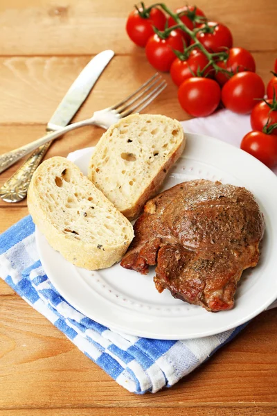 Roasted meat and vegetables on plate, on wooden table background — Stock Photo, Image