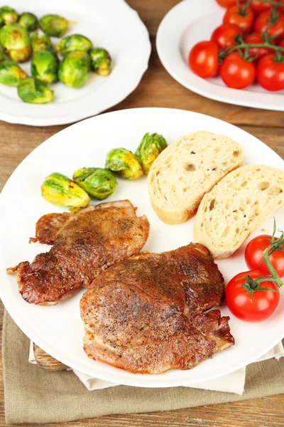 Carne asada y verduras en plato, sobre fondo de mesa de madera — Foto de Stock