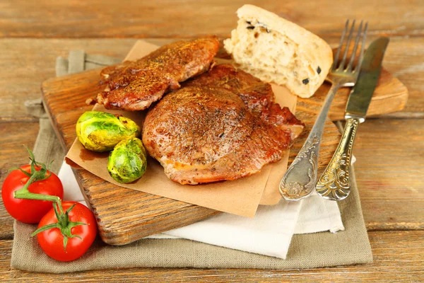 Viande rôtie et légumes sur planche à découper, sur fond de table en bois — Photo