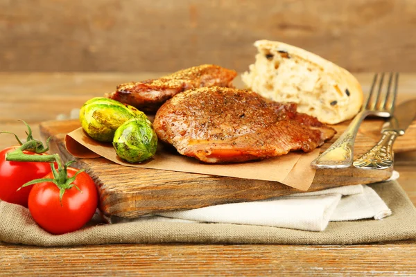 Carne asada y verduras sobre tabla de cortar, sobre fondo de mesa de madera — Foto de Stock