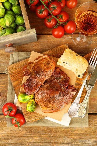 Roasted meat and vegetables on cutting board, on wooden table background — Stock Photo, Image