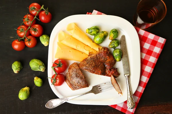 Roasted meat and vegetables on plate, on wooden table background — Stock Photo, Image