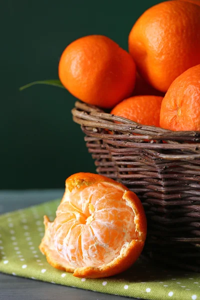 Fresh ripe mandarins in wicker basket, on wooden  table, on color background — Stock Photo, Image