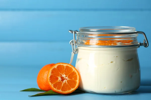 Tasty milk dessert with fresh tangerine pieces in glass jar, on color wooden background — Stock Photo, Image