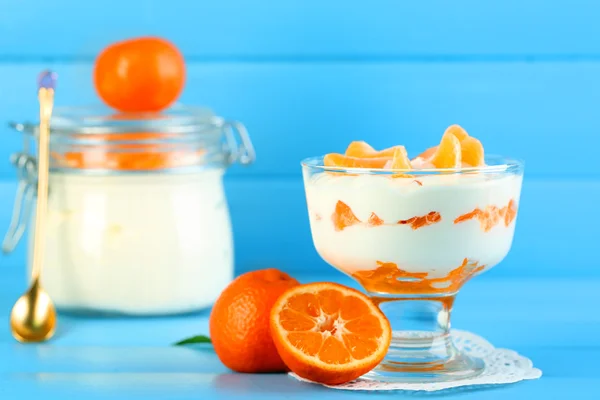 Dessert au lait savoureux avec des morceaux de mandarine fraîche dans un bol et un bocal en verre, sur fond de bois de couleur — Photo