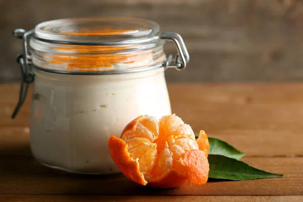 Tasty milk dessert with fresh tangerine pieces in glass jar, on  wooden background — Stock Photo, Image