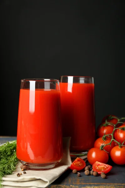 Vasos de sabroso jugo de tomate y tomates frescos sobre la mesa, sobre fondo gris —  Fotos de Stock