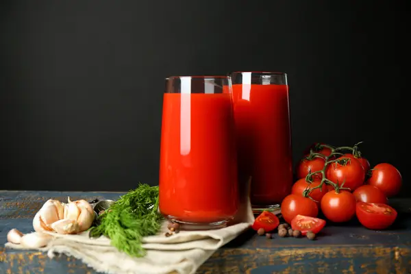 Vasos de sabroso jugo de tomate y tomates frescos sobre la mesa, sobre fondo gris — Foto de Stock