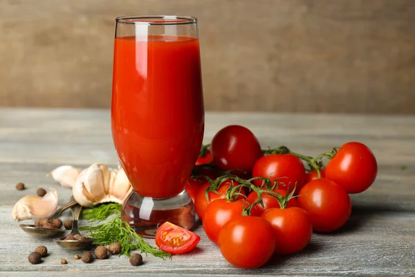 Vaso de sabroso jugo de tomate y tomates frescos sobre mesa de madera — Foto de Stock