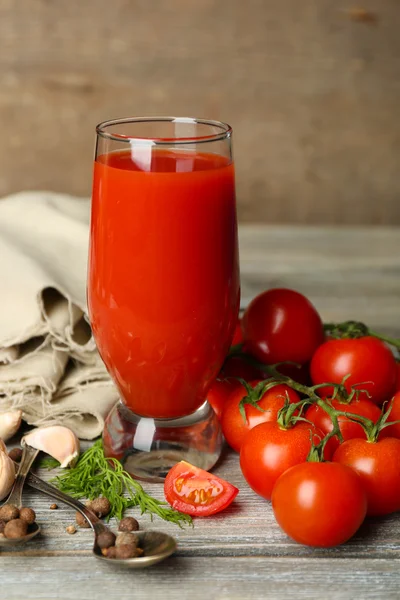 Vaso de sabroso jugo de tomate y tomates frescos sobre mesa de madera — Foto de Stock