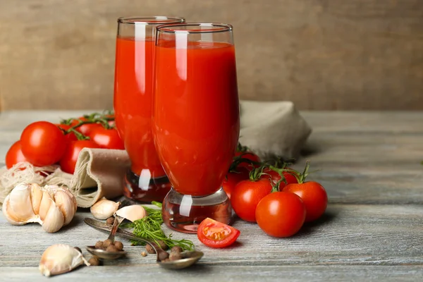 Vasos de sabroso jugo de tomate y tomates frescos en mesa de madera —  Fotos de Stock