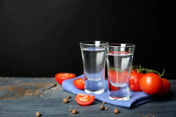 Glasses of ouzo and tomatoes on wooden table, on grey background — Stock Photo, Image